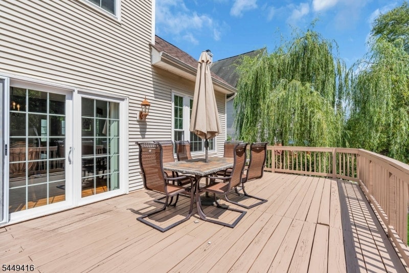 Furnished wooden deck with an outdoor dining set and leafy trees beyond the railing.