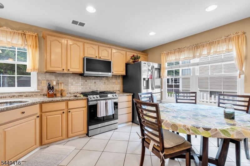 Kitchen with honey-colored cabinets, stainless steel appliances, and a dining table beside large windows.