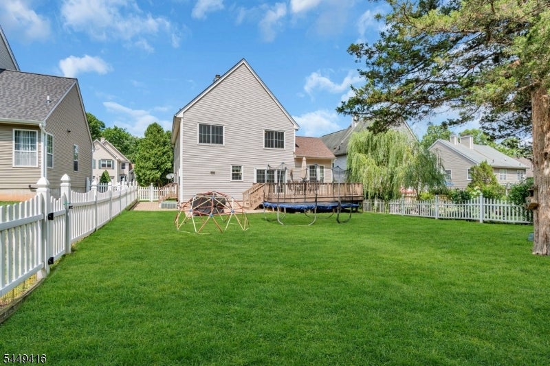 Two-story home with a wooden deck overlooking a fenced lawn with a swing set and trampoline.