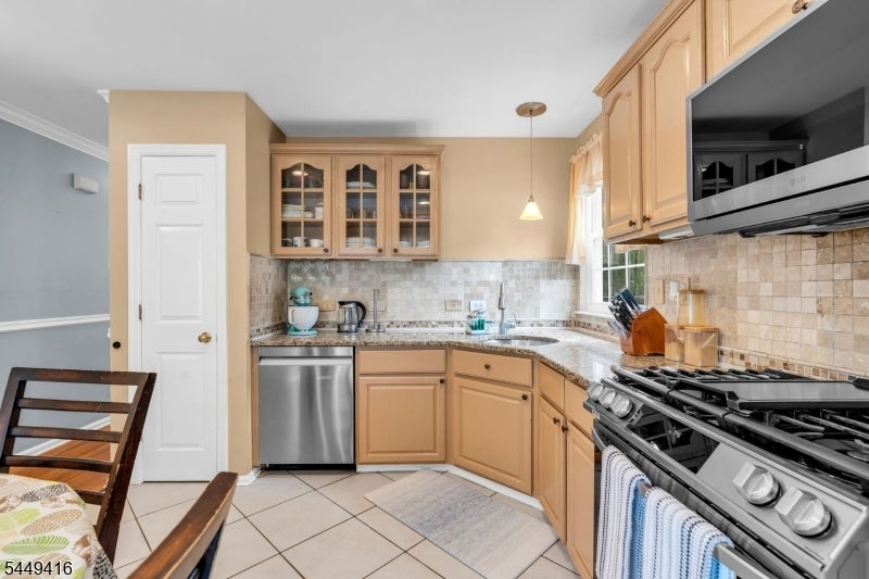 Kitchen with light wood cabinets, granite counters, tiled backsplash, and a large black range.