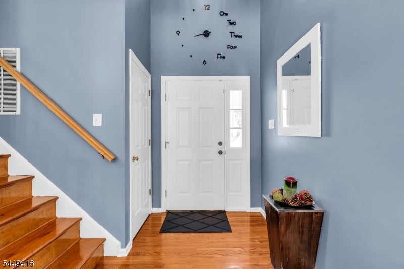 Entry foyer with blue walls, hardwood floors, a wooden staircase, and a white front door.