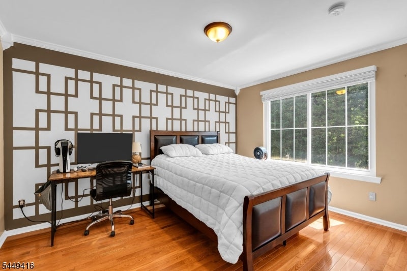 Bedroom with a large white bed, geometric accent wall, desk, and hardwood floors.