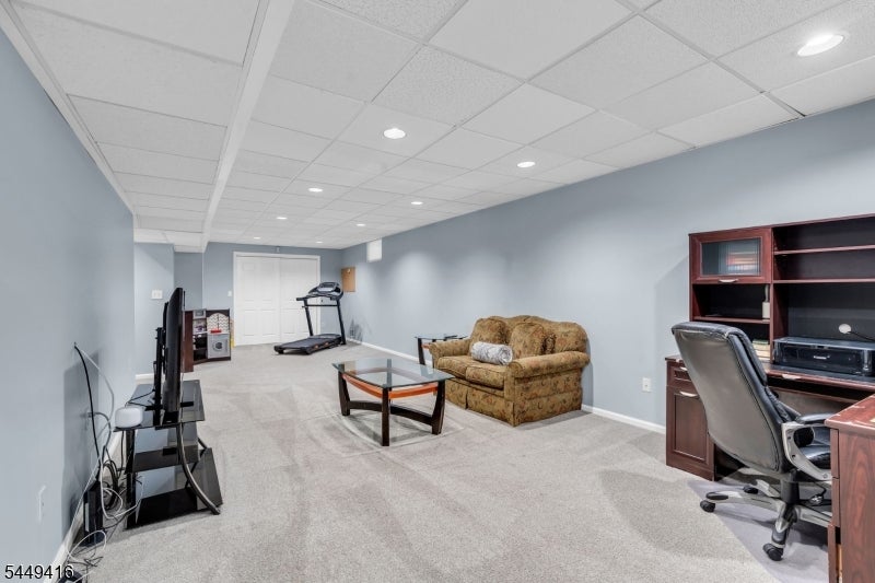 Finished basement with a sofa, glass coffee table, desk, television, and treadmill.