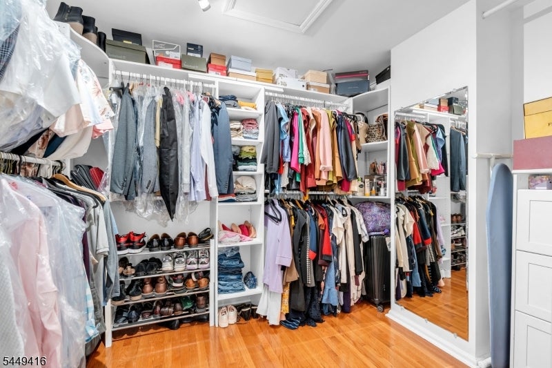 Walk-in closet with built-in shelving, extensive clothing storage, a full-length mirror, and hardwood floors.
