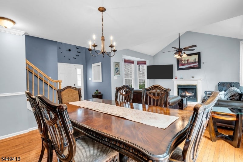 Dining and living area with a carved wood table, hardwood floors, staircase, and fireplace.