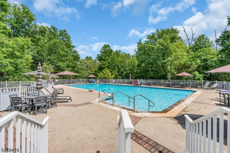 Outdoor swimming pool with a fenced deck, lounge chairs, and wooded surroundings.