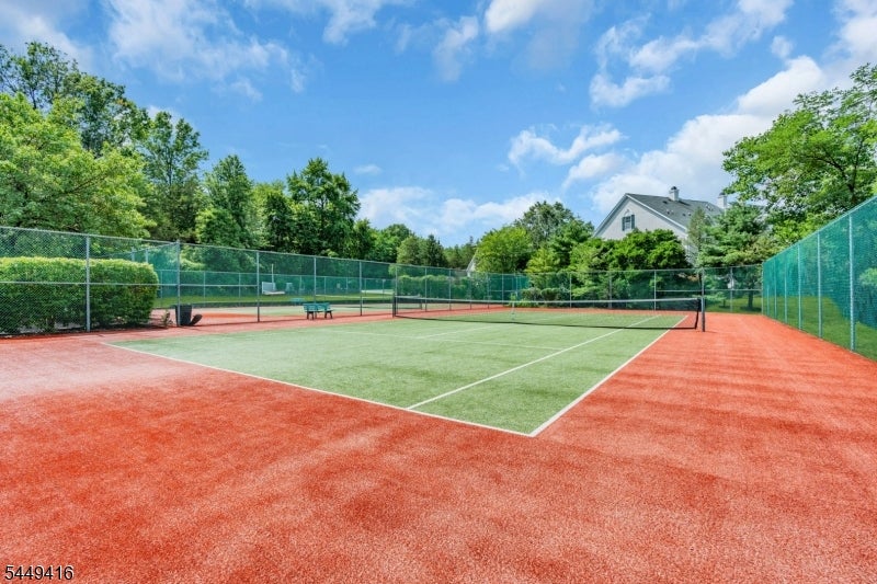 Outdoor tennis court with a green playing surface, red perimeter, and chain-link fencing.