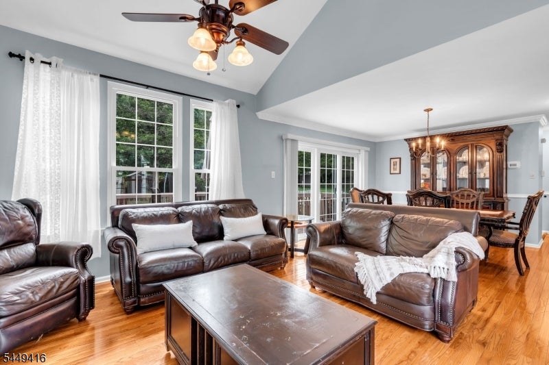 Living room with leather sofas, hardwood floors, and a vaulted ceiling opening to the dining area.