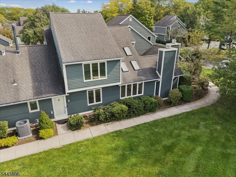 Green-sided multi-level home with gray shingle roofs, landscaped shrubs, and a curved sidewalk, viewed from above.