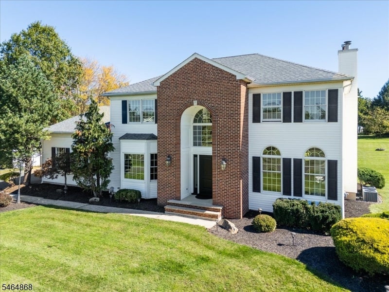 Two-story house with a red-brick entry, arched windows, black shutters, and a broad front lawn.