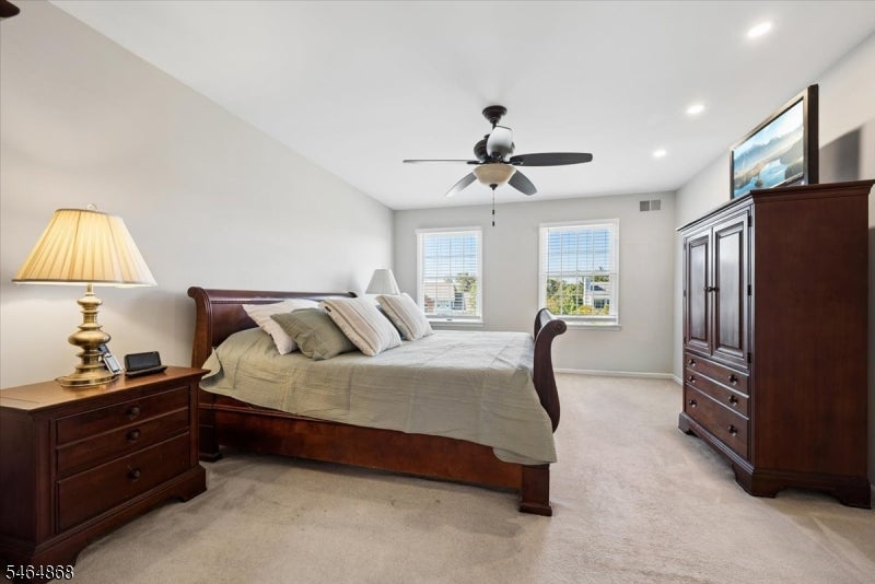 Furnished bedroom with a wooden bed, matching dresser, two windows, and a ceiling fan.