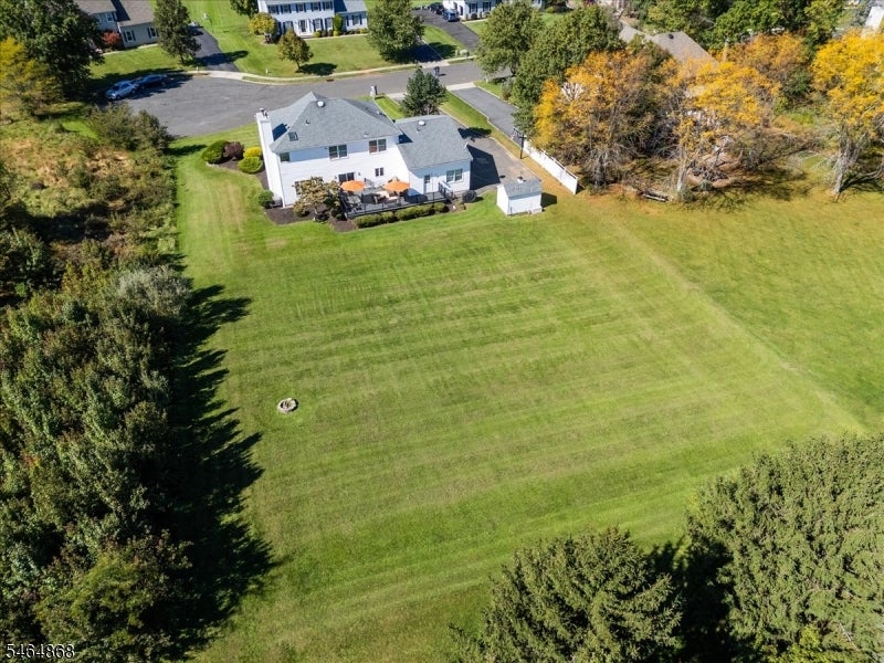 Aerial view of a white two-story house with a large lawn, rear deck, and detached shed.