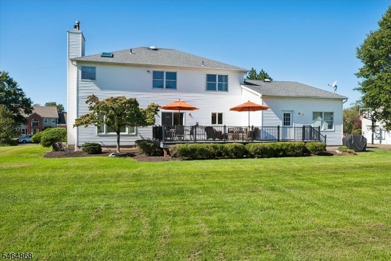 Rear of a white two-story home with a raised deck, orange umbrellas, and a broad green lawn.