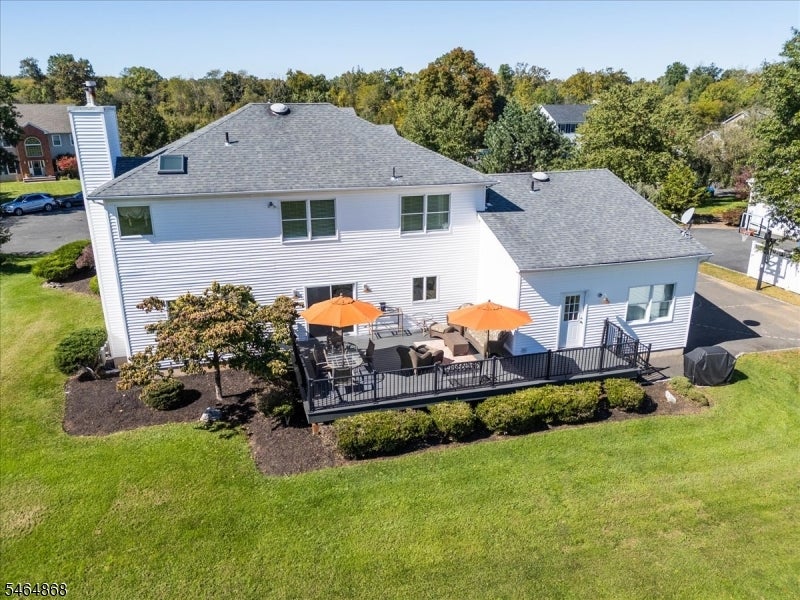 Aerial rear view of a white house with a deck, patio seating, and orange umbrellas.