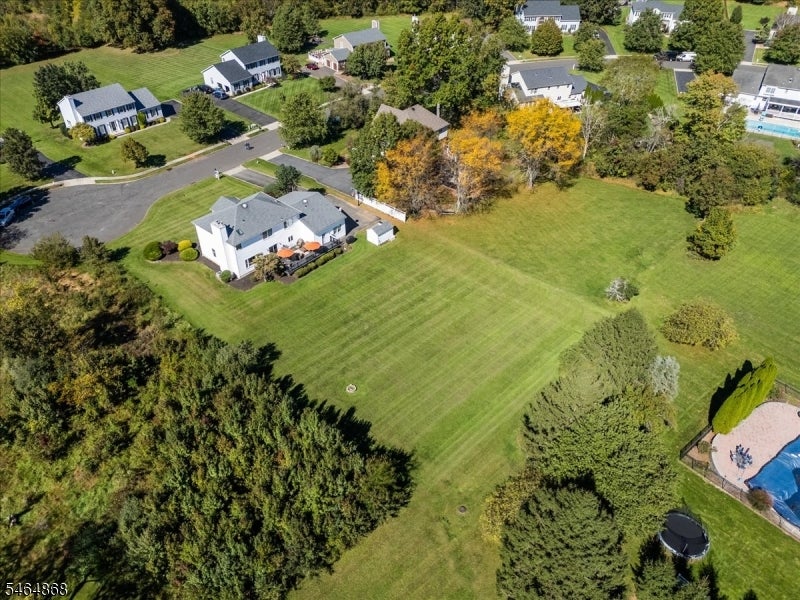 Aerial view of a home with a broad lawn, wooded edges, and a swimming pool.