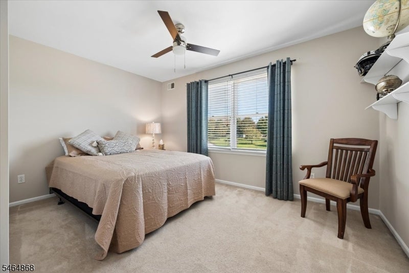 Furnished bedroom with a pale quilted bed, dark window curtains, and a wooden chair.
