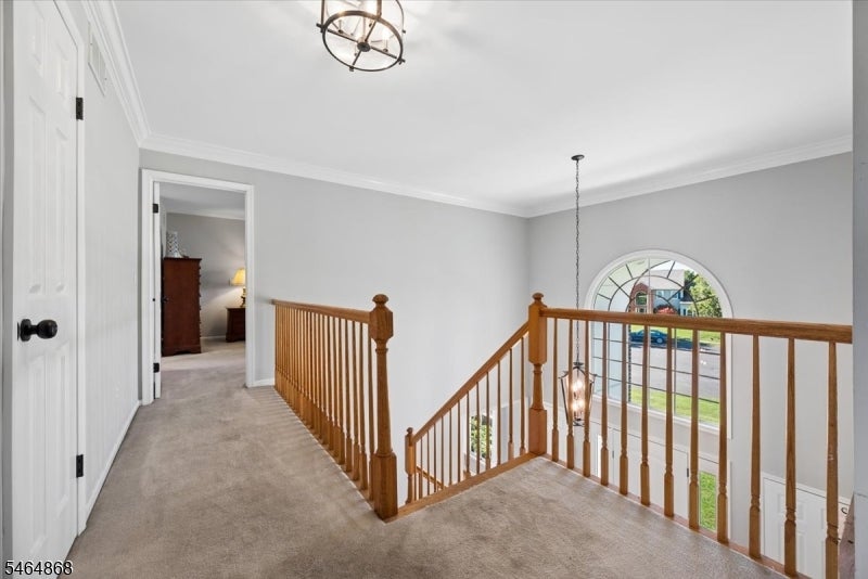 Upstairs landing overlooking a staircase with warm wood railings and a large arched window.