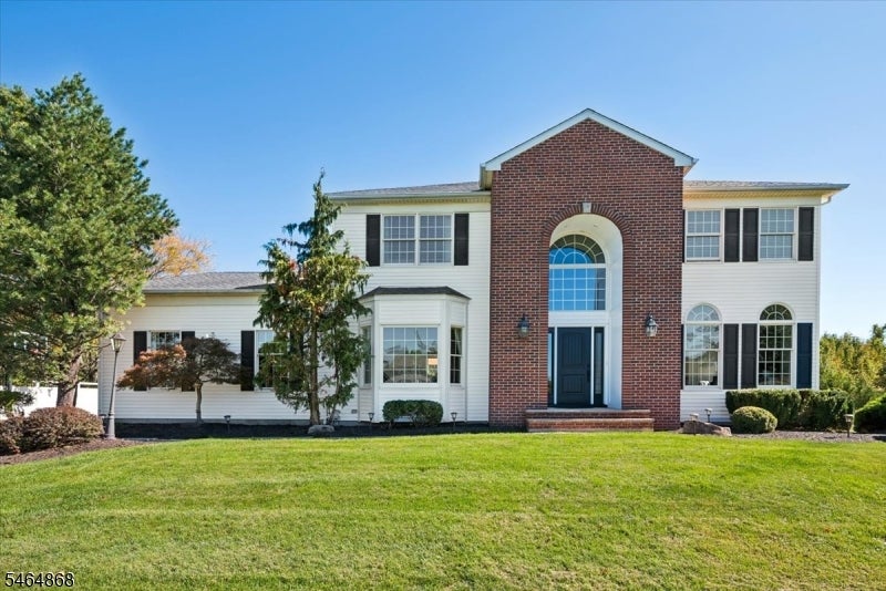 Two-story white-sided house with a prominent brick entry, black shutters, and a broad front lawn.