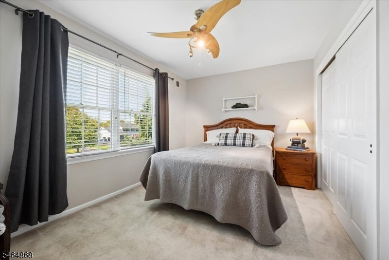 Bedroom with a centered bed, wide curtained window, wooden nightstand, and white closet doors.