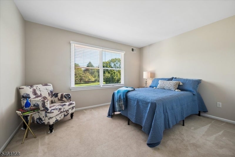 Bedroom with a blue-covered bed, floral armchair, and wide window overlooking greenery.