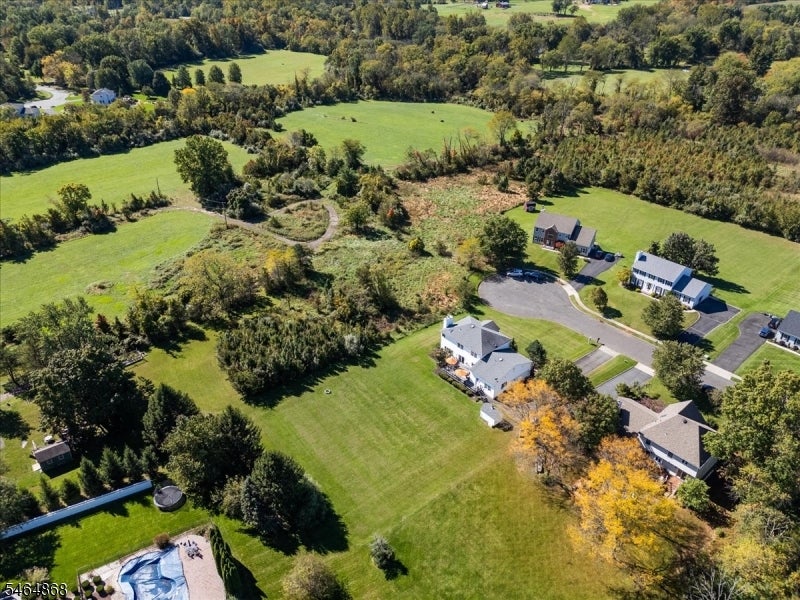 Aerial view of a home with broad lawns, wooded surroundings, and nearby houses.