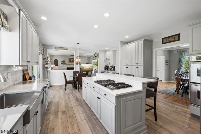 Kitchen with a large white island, gas cooktop, stainless steel appliances, and wood floors.
