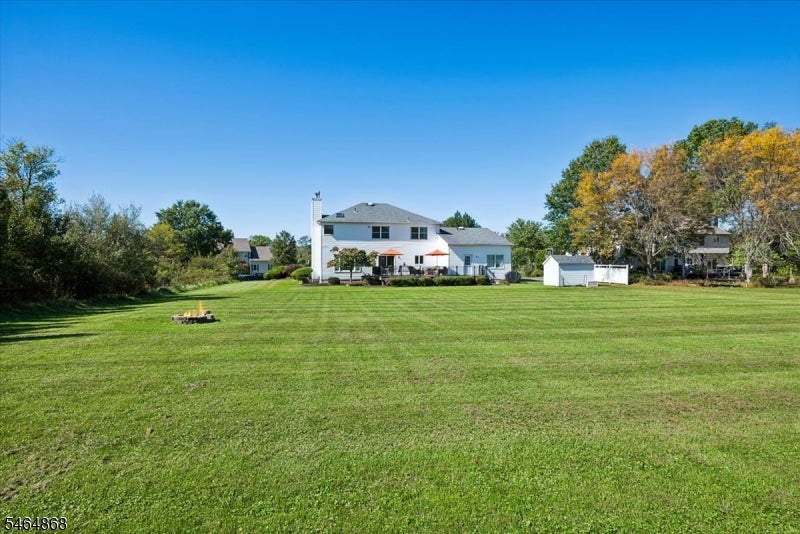 White two-story house beyond a broad lawn, with a patio, small outbuilding, and autumn trees.