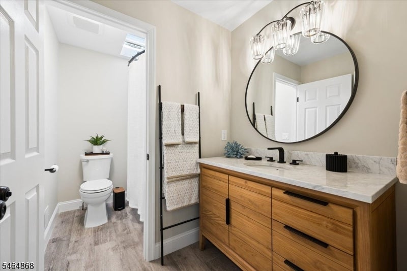 Bathroom with a wood vanity and round mirror beside a separate toilet alcove.