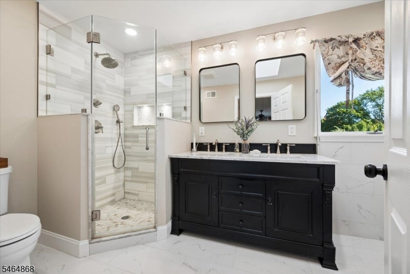 Bathroom with a glass-enclosed tiled shower, black vanity, marble-look flooring, and a window overlooking trees.