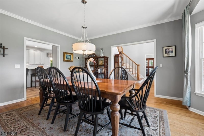Dining room with a wooden table, black chairs, chandelier, and adjoining kitchen and staircase.