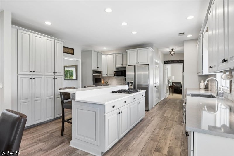 Bright kitchen with white cabinetry, a large cooktop island, stainless steel appliances, and wood-look floors.