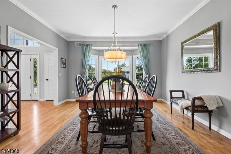 Dining room with a long wooden table, spindle-back chairs, and large curtained windows.