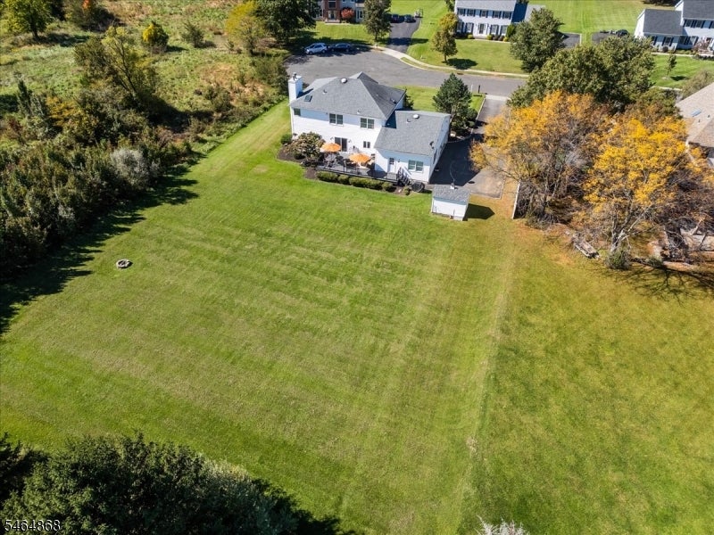 Aerial view of a white two-story house overlooking a broad lawn, with a rear patio and tree-lined edges.