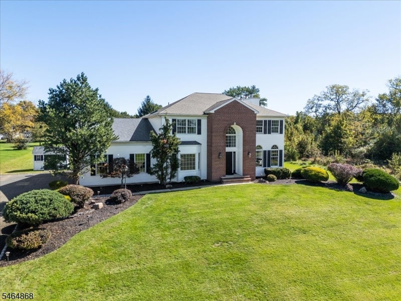 Two-story white house with a red-brick entrance, landscaped lawn, and mature trees.