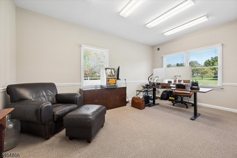 Office with a computer workstation, black leather sofa and ottoman, and windows overlooking a lawn.