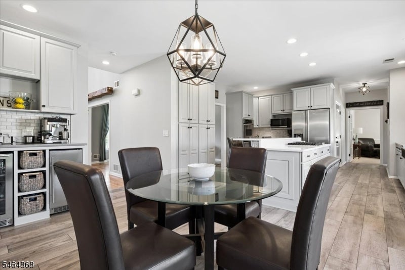 Dining area with a round glass table and dark chairs beside a white kitchen with stainless steel appliances.