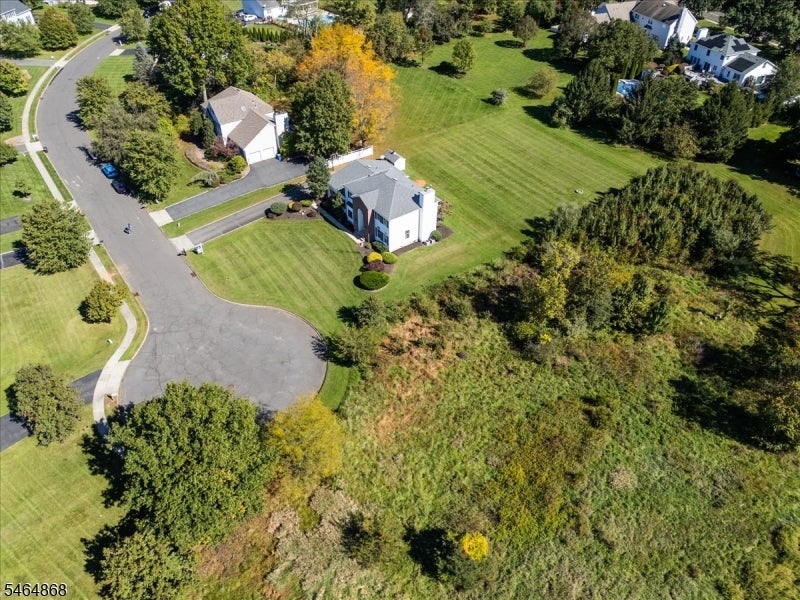 Aerial view of a white two-story home beside a curved road, broad lawn, and wooded land.