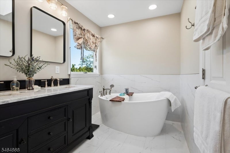 Bathroom with a freestanding soaking tub beside a dark vanity and marble-look tile.