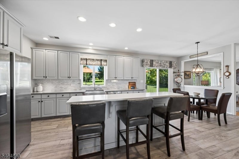Kitchen with gray cabinets, stainless appliances, and a large island with dark stools beside the dining area.