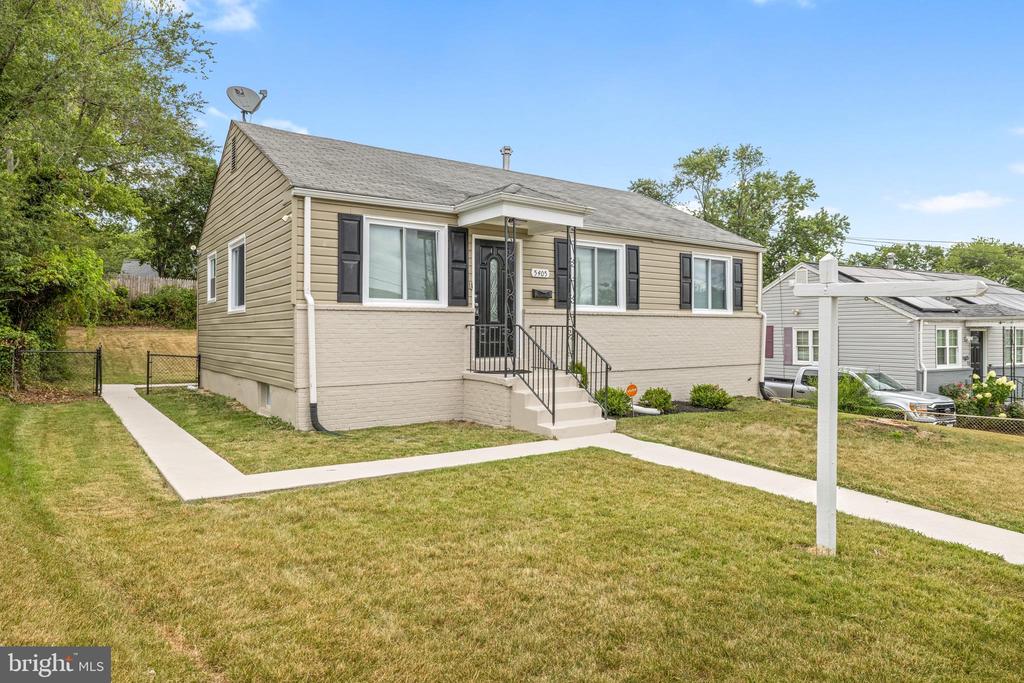 Beige single-story house with dark shutters, front steps, and a concrete walkway across the lawn.