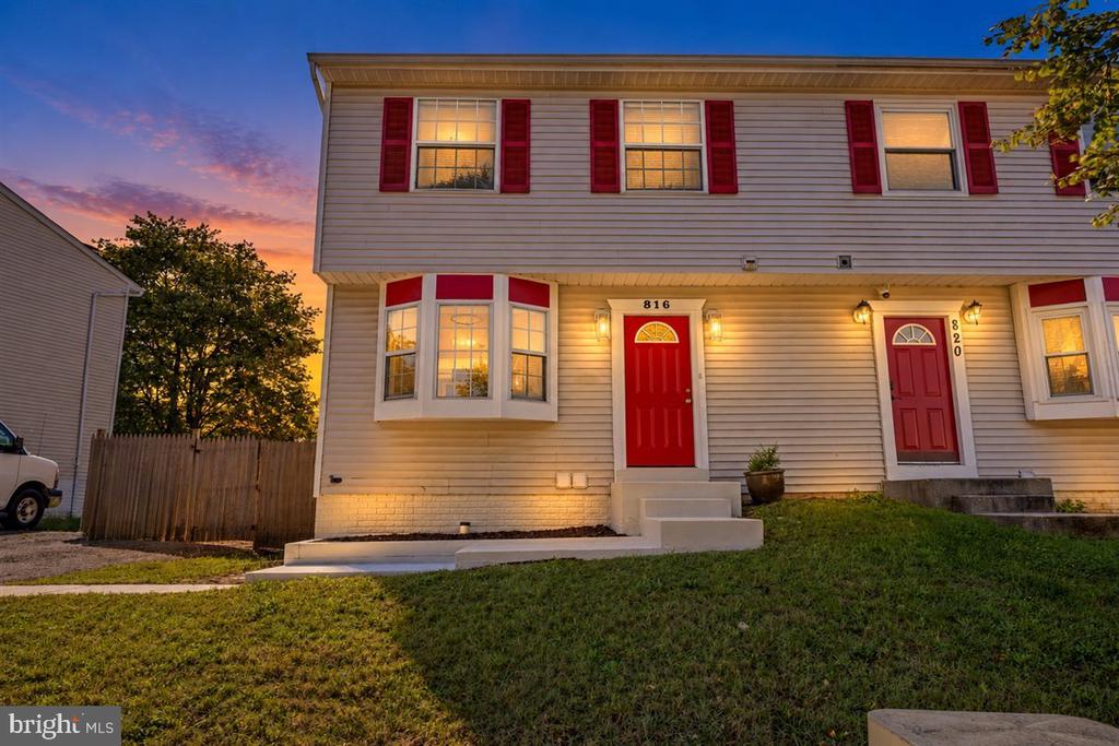 Two-story residence with red doors and shutters, warmly lit at dusk beneath a colorful sunset sky.