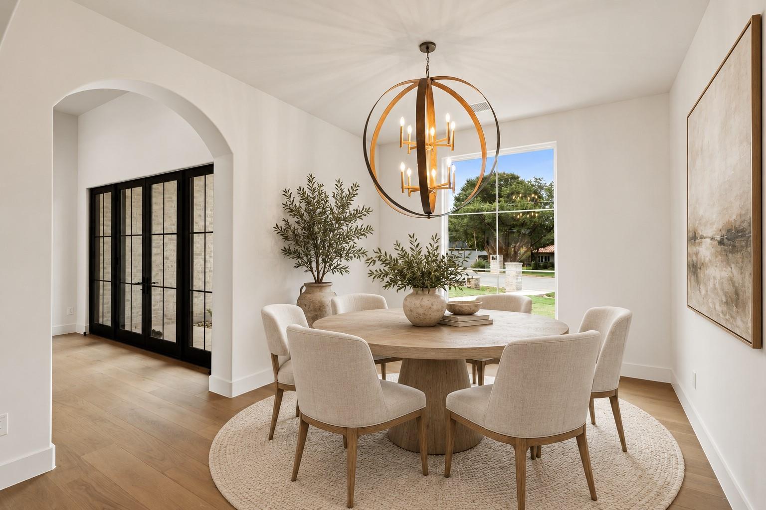 Dining room with a round wood table, upholstered chairs, and a sculptural brass chandelier.