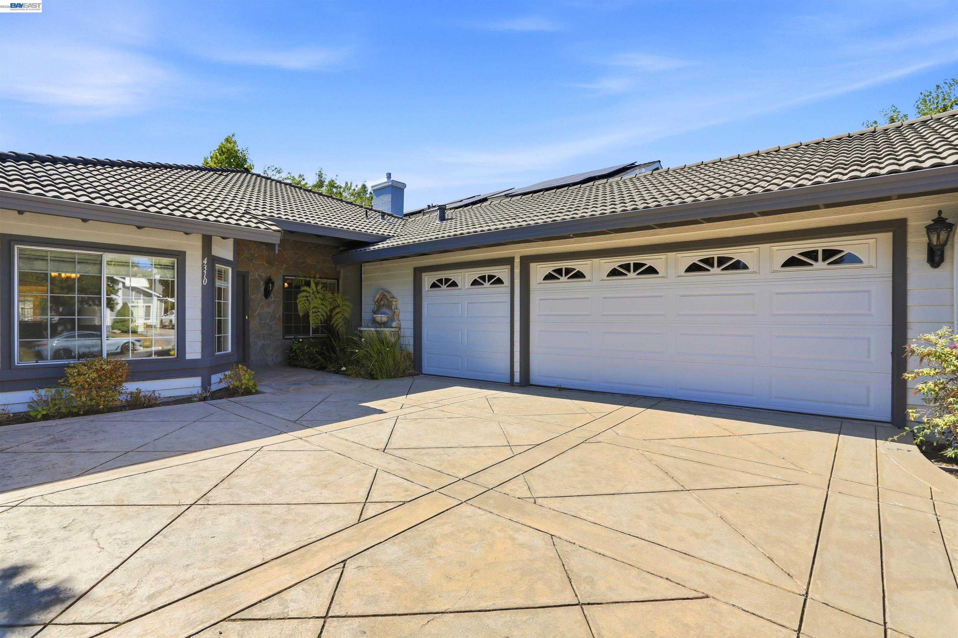 Home exterior with a broad stamped-concrete driveway, two garage doors, and solar panels.