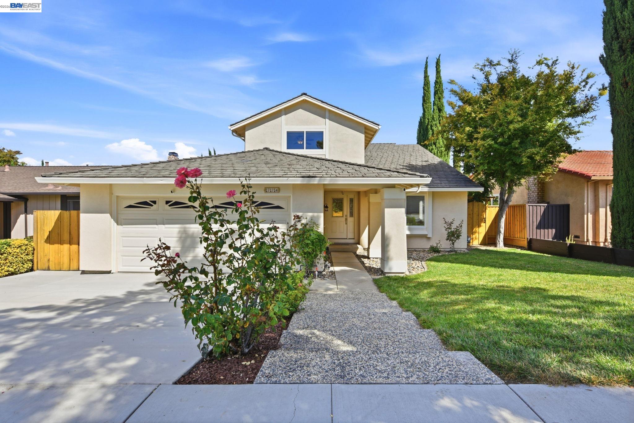 Two-story stucco home with a double garage, pebble walkway, and landscaped front lawn.
