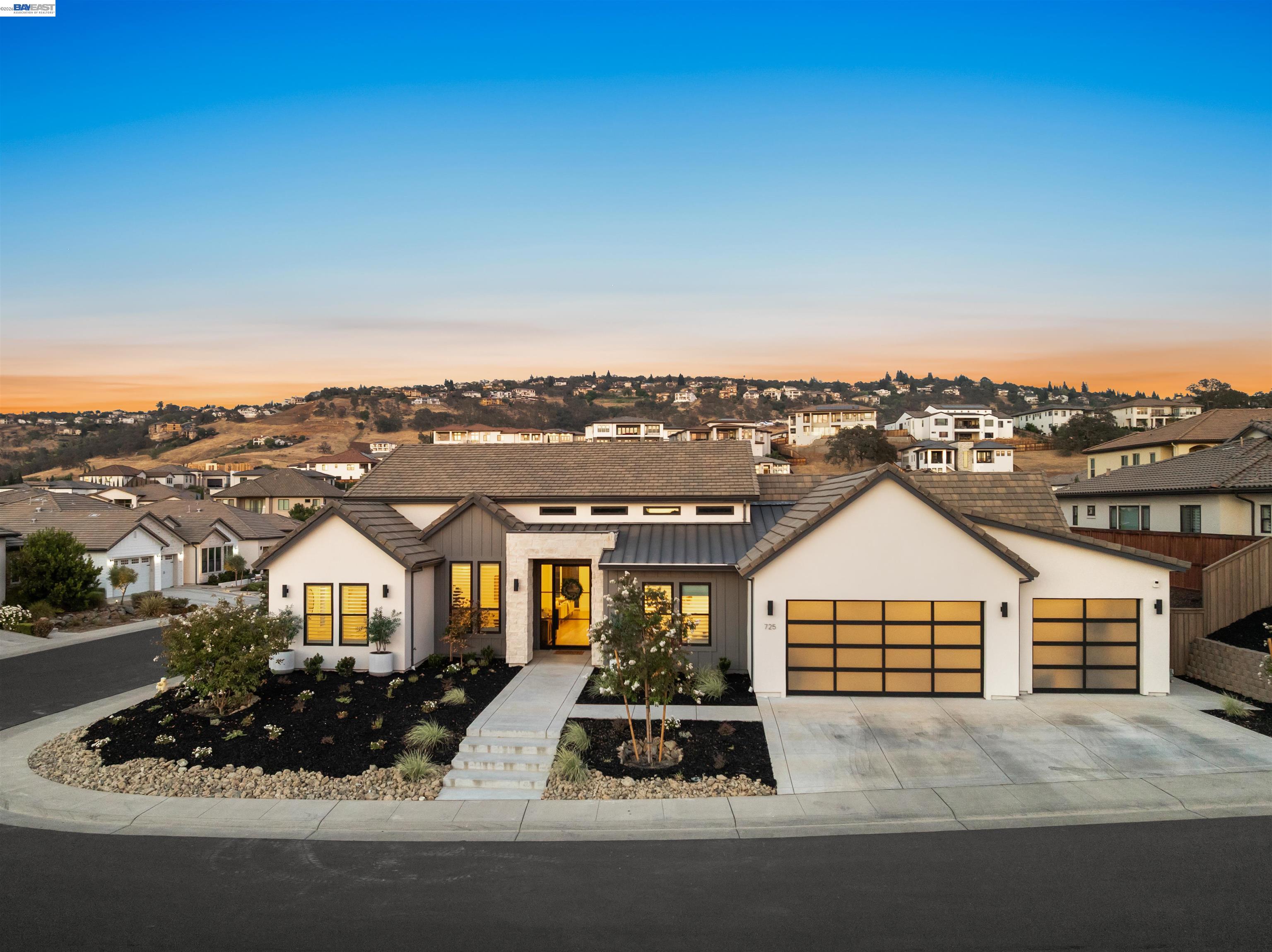 Modern white home with two garage doors and landscaped front yard at golden hour.