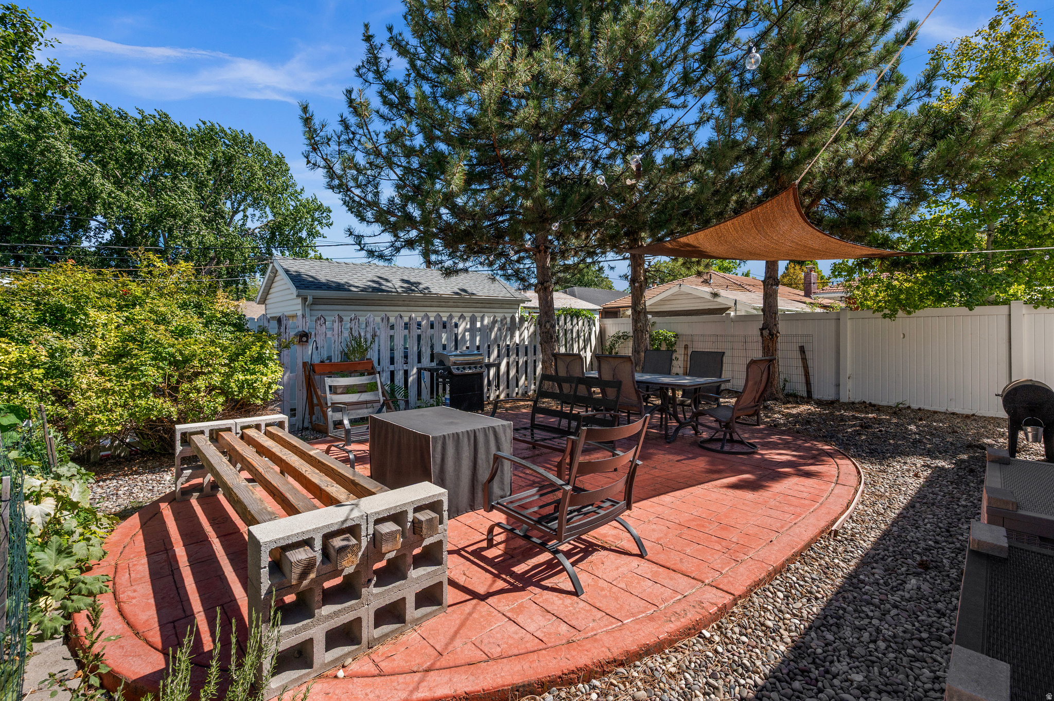 Backyard patio with red brick pavers, outdoor dining furniture, a grill, and a shade sail.