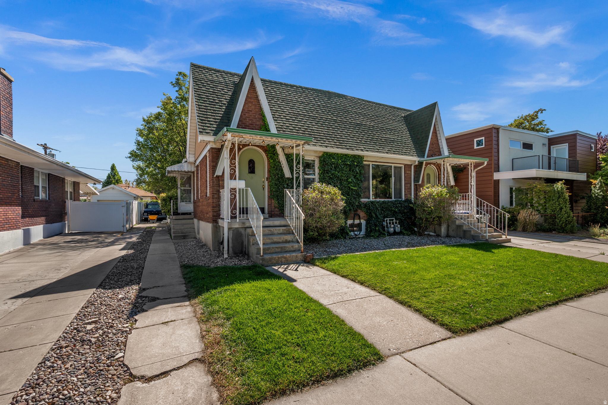 Brick Tudor-style duplex with steep gables, ivy-covered walls, and a small front lawn.