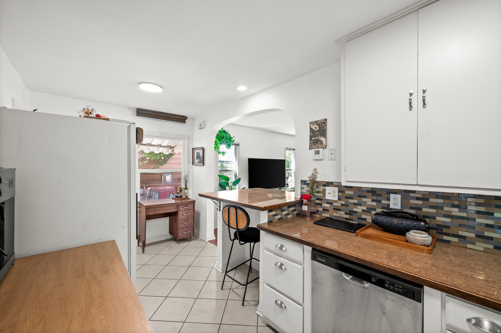 Kitchen with brown countertops, colorful tile backsplash, white cabinets, and a breakfast bar.