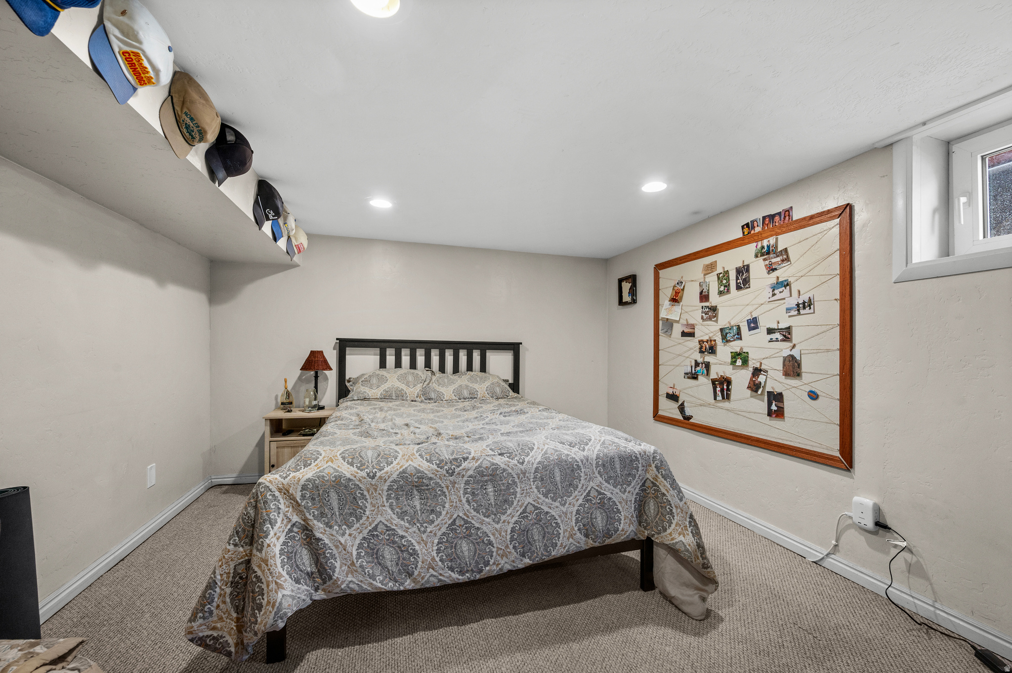 Furnished bedroom with patterned bedding, a photo display, and baseball caps along a ceiling ledge.