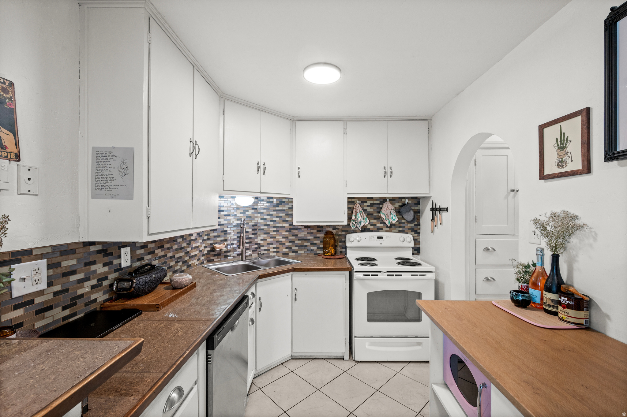 Kitchen with white cabinets, multicolored tile backsplash, brown counters, and an electric range.